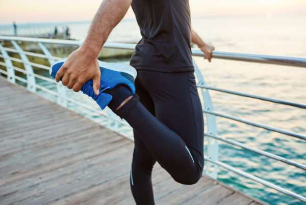 Un uomo ibnforma fa lo stretching della gamba guardando il mare